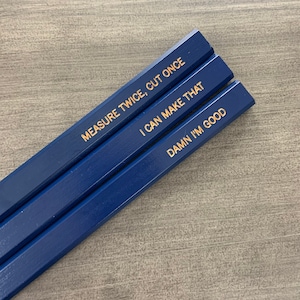 May include: Three blue pencils with gold lettering. The pencils have the following sayings: "Measure twice, cut once", "I can make that", and "Damn I'm good".
