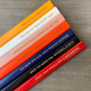 May include: A set of eight custom pencils with different coloured wood and gold lettering. The pencils have various sayings on them, including "This is a custom pencil", "You can put your quote here", "Swearwords? Accent marks? We got you", "You know who loves pencils? Carpenters", "You know who else loves pencils? Everyone", "Great for marketing, weddings, & gifts", and "Create your pencils now & #getwriting".