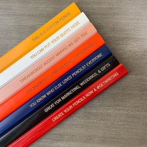 May include: A stack of eight custom pencils with different coloured wood and gold lettering. The pencils have various sayings on them, including "This is a custom pencil", "You can put your quote here", "Swearwords? Accent marks? We got you", "You know who loves pencils? Carpenters", "You know who else loves pencils? Everyone", "Great for marketing, weddings, & gifts", and "Create your pencils now & #getwriting".