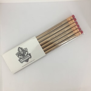 May include: A set of six gold pencils with red erasers. Each pencil is engraved with the text "Lucky Bar Exam Pencil". The pencils are packaged in a white envelope with a logo for "The Carbon Crusader" and a website address.