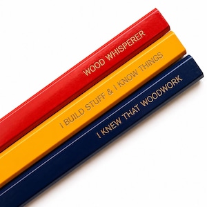 Könnte beinhalten: Drei sechseckige Stifte in Rot, Gelb und Dunkelblau, jeweils mit goldfarbenem Text versehen. Der rote Stift trägt die Aufschrift WOOD WHISPERER, der gelbe I BUILD STUFF & I KNOW THINGS und der dunkelblaue I KNEW THAT WOODWORK.