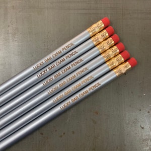 May include: Six silver pencils with red erasers and gold accents. Each pencil is engraved with the text "LUCKY BAR EXAM PENCIL".