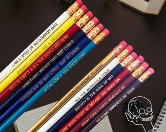 May include: A collection of pencils in various colors, each inscribed with quotes from Shakespeare. The pencils have pink erasers and gold-colored metal bands. The quotes are in gold lettering and include phrases like "Double, double toil & trouble."