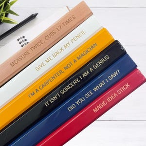 May include: A set of six wooden pencils with different colored paint and humorous sayings printed in gold lettering. The sayings are: "Measure twice, cuss 17 times", "Give me back my pencil", "I'm a carpenter, not a magician", "It isn't sorcery, I am a genius", "Did you see what I saw?", and "Magic idea stick".