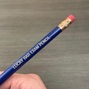 May include: A blue pencil with a pink eraser and gold lettering that reads "LUCKY BAR EXAM PENCIL".