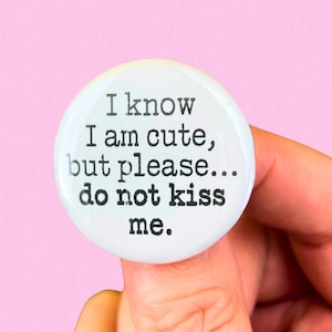 Puede incluir: Botón blanco con texto negro que dice "Sé que soy lindo, pero por favor... no me beses."