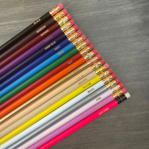 May include: A set of 18 wooden pencils with different colored paint and gold lettering. The pencils are labeled with the color of the paint: black, maroon, brown, purple, dark blue, navy, aqua, red, orange, gold, cream, natural, yellow, white, silver, pink, lavender, and hot pink.
