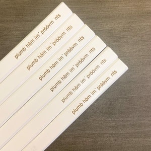 May include: Six white pencils with gold lettering that reads "plumb hom im prōōvm nts".