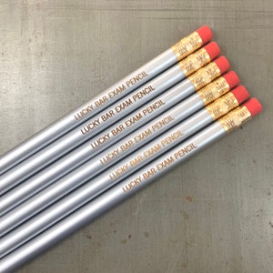 May include: Six silver pencils with red erasers and gold accents. Each pencil is engraved with the text "LUCKY BAR EXAM PENCIL".