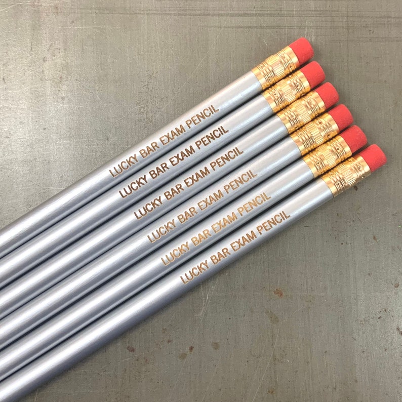 May include: Six silver pencils with red erasers and gold accents. Each pencil is engraved with the text "LUCKY BAR EXAM PENCIL".