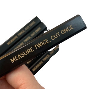 Puede incluir: Un juego de cuatro lápices negros con letras doradas que dicen "MEASURE TWICE, CUT ONCE".