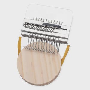 May include: A weaving tool with a light wood circular base and a metal frame. The frame has a series of hooks and a spring mechanism. The tool is designed for creating woven crafts.