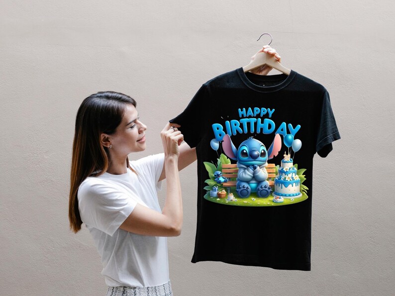 Puede incluir: Camiseta negra con un personaje de dibujos animados azul y la frase "HAPPY BIRTHDAY". El dise&ntilde;o incluye globos y una tarta de cumplea&ntilde;os. La camiseta la sostiene una persona.