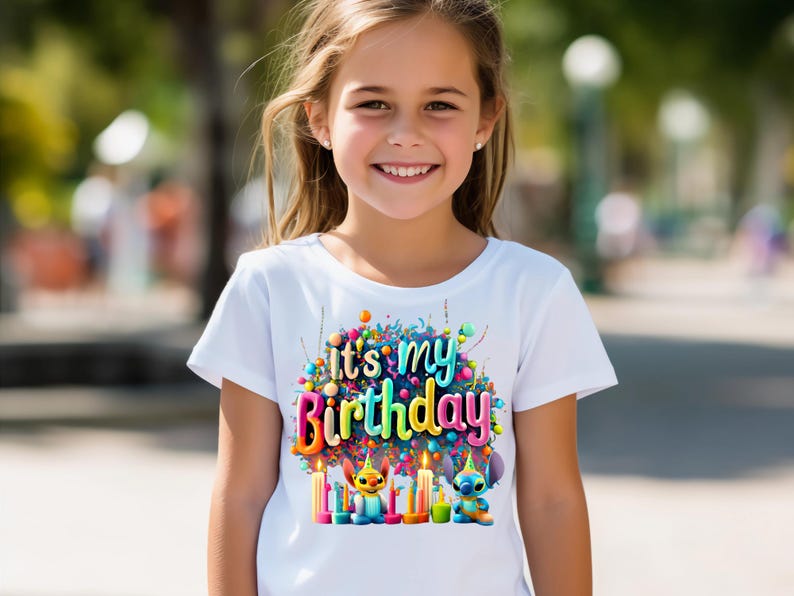 Puede incluir: Camiseta blanca con un gr&aacute;fico colorido que dice "It's my Birthday". El dise&ntilde;o incluye velas, globos y personajes de dibujos animados. La camiseta la lleva una ni&ntilde;a.
