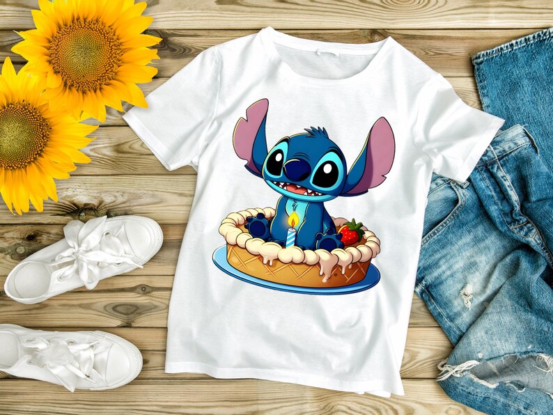 Puede incluir: Camiseta blanca con un personaje de dibujos animados, Stitch, sentado en una tarta con una vela encendida y una fresa. La imagen est&aacute; sobre una superficie de madera con girasoles, zapatillas blancas y vaqueros.