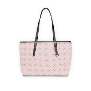 Può includere: Una borsa tote rosa con un motivo a piccoli cuori verdi. La borsa ha manici e finiture nere, con fibbie color oro e un anello a D. La borsa è progettata per essere portata a spalla.