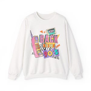 Può includere: Felpa bianca con un design grafico colorato. Il design presenta un telefono cellulare rosa, una musicassetta e il testo "BACK TO THE 90'S" in colori vivaci. La felpa ha un girocollo e maniche lunghe.