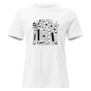 Può includere: T-shirt bianca con grafica in bianco e nero di libri e fiori. I libri presentano dettagli a forma di stelle e cuori. La maglietta è realizzata in un materiale morbido, ideale per l'uso quotidiano.