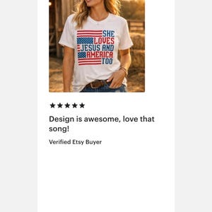 May include: White t-shirt with a patriotic design. The shirt features the text "She Loves Jesus and America Too" in blue and red, with American flag elements. The shirt is worn by a person.