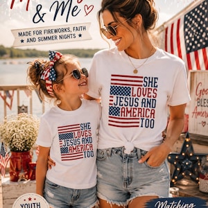 May include: A mother and child wearing matching white t-shirts with an American flag design and the text "She Loves Jesus and America Too." The image is themed around patriotism and family, with fireworks in the background.