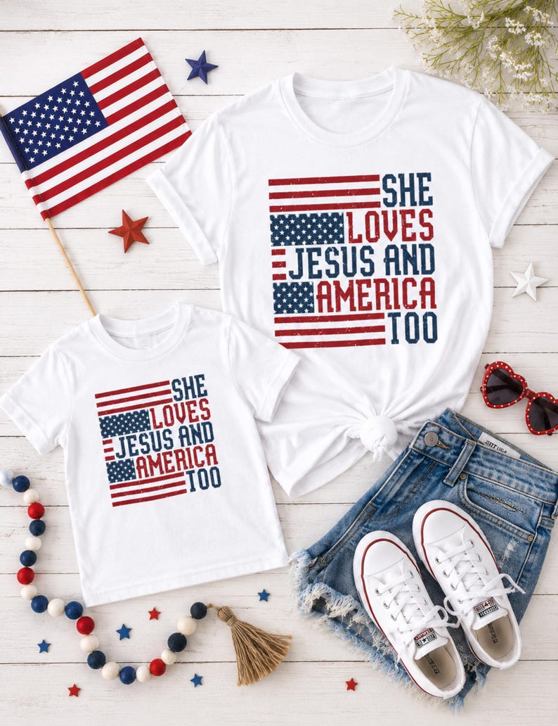 May include: Two white t-shirts with the text "SHE LOVES JESUS AND AMERICA TOO" in red and blue, designed to resemble the American flag. The shirts are paired with denim shorts, white sneakers, and patriotic decorations.