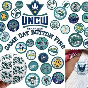 May include: A collection of teal and white game day button pins with various designs and text, including "UNCW Seahawks," "Wings Up," and a smiley face. One pin is attached to a person's clothing.