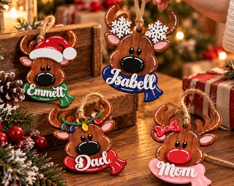 May include: Four wooden reindeer ornaments with jute twine hangers. Each features a brown reindeer face with a unique accessory: a Santa hat, white snowflakes, colorful Christmas lights, or a red bow. Each wears a scarf with a name: Emmett, Isabell, Dad, or Mom.