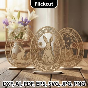 Może przedstawiać: Trzy drewniane dekoracje wielkanocne w kształcie jajek z misternymi wzorami wyciętymi laserowo. Każde jajo przedstawia inną scenę: królika, kwiaty i kosz. Jajka stoją na drewnianych podstawkach. Obraz zawiera tekst "Flickcut" i opcje typu pliku.