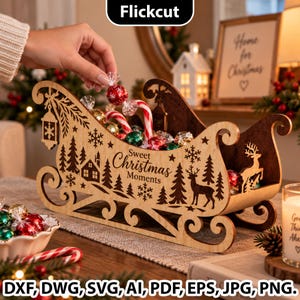 Puede incluir: Un trineo decorativo de madera con diseños cortados a láser de pinos, copos de nieve, una casa y un reno. El lateral está grabado con el texto Sweet Christmas Moments. El trineo está lleno de caramelos envueltos y bastones de caramelo.