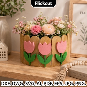 May include: A cylindrical wooden planter featuring a picket fence design with three pink tulip cutouts and green leaves attached to the front. The planter is filled with a variety of pink, peach, and white artificial flowers. The text Flickcut is visible at the top, and DXF, DWG, SVG, AI, PDF, EPS, JPG, PNG are listed at the bottom.