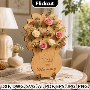 Könnte beinhalten: Ein hellbrauner Blumenständer aus Holz mit einem gewellten oberen Rand und mehreren Löchern für Stiele. Die Basis ist mit dem Text PICKED FOR Mommy graviert. Der Ständer enthält mehrere rosa und weiße Rosen sowie Zweige von Schleierkraut.