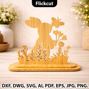 Puede incluir: Silueta de conejo de madera con mariposa y detalles florales. El conejo sostiene flores, y la base tiene dos niveles. La imagen incluye el texto "Flickcut" y opciones de formato de archivo: DXF, DWG, SVG, AI, PDF, EPS, JPG, PNG.