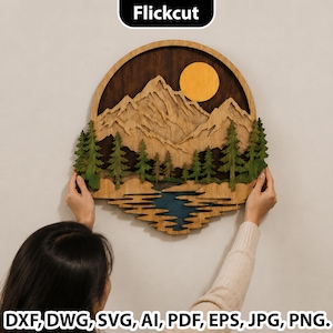 May include: A circular wooden wall art piece featuring a layered mountain landscape with a yellow sun, green pine trees, and a blue lake. The design includes the text Flickcut at the top and DXF, DWG, SVG, AI, PDF, EPS, JPG, PNG at the bottom.