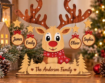 May include: A wooden reindeer decoration featuring a red nose and scarf, with four hanging circular ornaments engraved with the names James, Emily, Oliver, and Sophia. The base is engraved with The Anderson Family and two small hearts.