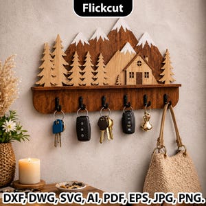 May include: Wooden key holder with a mountain and cabin design. The key holder has a dark brown finish with black hooks. The mountains have white accents. Keys and a purse hang from the hooks. The text "Flickcut" is at the top.