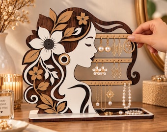May include: A wooden jewelry display stand shaped like a woman's profile with floral hair details. It features horizontal bars with holes for hanging earrings and a base tray for rings and necklaces. The design is dark brown and cream colored.