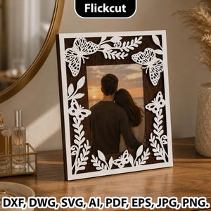 May include: A rectangular picture frame featuring a dark brown wood-toned inner border and a white outer frame layer with intricate laser-cut butterfly and leafy vine designs. The frame displays a photograph of two people embracing at sunset.