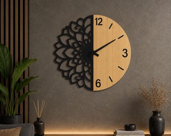 Può includere: Un orologio da parete circolare dal design diviso. La metà sinistra presenta un motivo mandala nero tagliato al laser, mentre la metà destra ha una finitura in legno chiaro con i numeri neri 3, 6 e 12. Lancette nere posizionate al centro.
