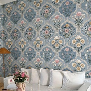 May include: A living room with a white sofa, a wooden coffee table, and a patterned blue wallpaper. The coffee table has books, a vase of flowers, and candles. The rug is beige with a scalloped edge.