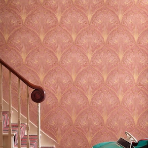May include: A room with pink wallpaper featuring a repeating gold fan design. A staircase with a patterned runner and a teal toy car are in the foreground. The wallpaper adds a vintage touch to the space.