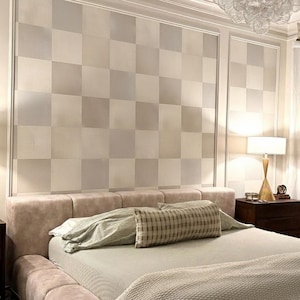 May include: A bedroom with a large bed, featuring a light pink, plush headboard and frame. The bed is made with neutral-toned bedding and decorative pillows. The wall behind the bed has a checkered pattern in shades of beige and grey.