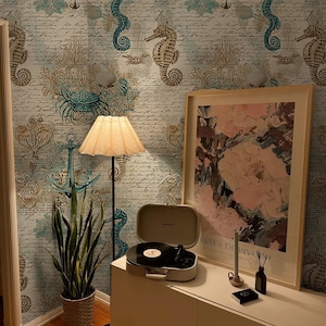 Puede incluir: Una habitación con papel pintado de caballitos de mar en azul claro y beige. Se ve una impresión floral enmarcada, un tocadiscos, una lámpara de pie y una planta en maceta. El papel pintado tiene caballitos de mar, anclas y escritura.