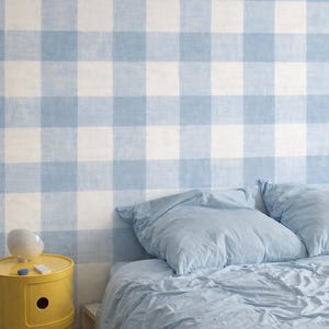 Può includere: Una camera da letto con una parete a quadri blu e bianchi. Un comodino giallo con tre cassetti è a sinistra, e un letto con lenzuola e cuscini blu è a destra. Un oggetto decorativo bianco è appoggiato sul tavolo.