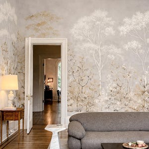 Puede incluir: Un salón con un sofá gris, una mesa de centro negra y una pequeña mesa auxiliar de madera con una lámpara. Las paredes presentan un mural con temática de la naturaleza con árboles en tonos dorados y blancos. Una puerta conduce a otra habitación.