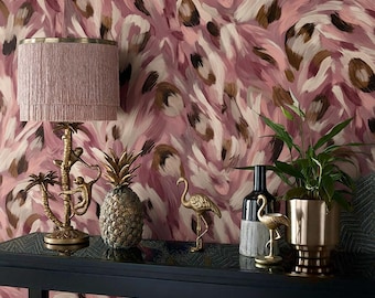 May include: A decorative display featuring a pink fringed lampshade, a gold pineapple, and a gold flamingo figurine. The items are arranged on a black table against a pink and brown abstract patterned wallpaper.