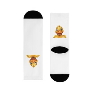 Könnte beinhalten: Weiße Socken mit schwarzen Fersen und Zehen. Jede Socke zeigt ein Cartoon-Entengesicht in Gelb, Orange und Braun. Eine Ente ist aufrecht, die andere ist verkehrt herum. Die Socken sind ein lustiges und skurriles Accessoire.