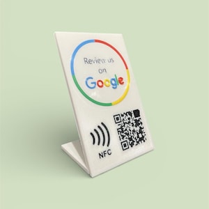 Könnte beinhalten: Ein weißes, abgewinkeltes Schild mit dem Google-Logo und dem Text "Review us on Google". Es verfügt über einen QR-Code und ein NFC-Symbol. Das Schild ist so konzipiert, dass es aufrecht steht.