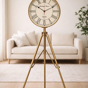 Könnte beinhalten: Eine goldfarbene Uhr im Vintage-Stil auf einem Stativ. Das Zifferblatt ist cremefarben mit schwarzen römischen Ziffern und Zeigern. Die Uhr zeigt "Huntleigh Station, Cambridge England 1924".