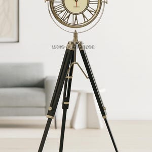 Peut inclure: Une horloge de sol décorative avec un cadran rond et des chiffres romains, montée sur un trépied noir. Le cadran est crème avec des aiguilles noires et le texte "Franklin & Murphy, Est. 1884, Oxford". Le cadre de l'horloge est métallique.