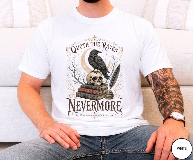 Puede incluir: Una camiseta blanca con un estampado gr&aacute;fico de un cuervo negro posado sobre un cr&aacute;neo humano, que descansa sobre una pila de tres libros. Junto a los libros hay un tintero con una pluma. El texto dice Quoth the Raven Nevermore Once upon a midnight dreary.